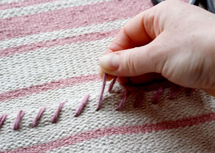 someone is knitting on a striped blanket with pink yarn and crochet hooks in front of them