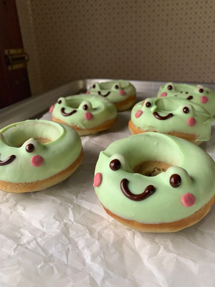 donuts with green frosting and pink sprinkles are on a sheet of wax paper