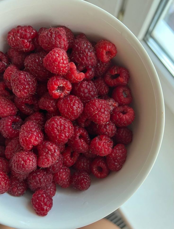 a white bowl filled with raspberries on top of a table