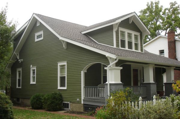 a green house with white trim on the front porch and two story windows, surrounded by greenery