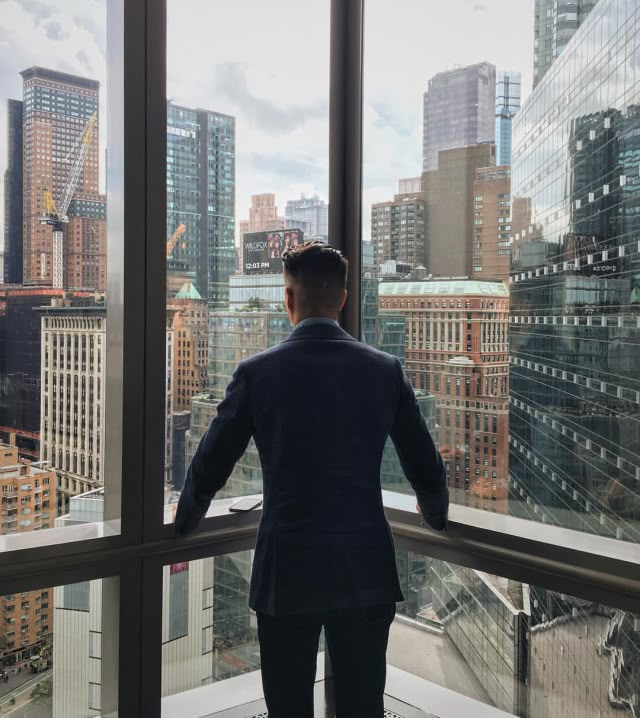 a man standing in front of a window looking out at the cityscape and skyscrapers