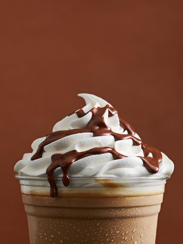 a chocolate drink with whipped cream and drizzled on top is sitting in front of a brown background