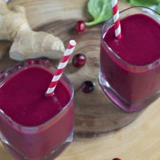 two glasses filled with cranberry juice on top of a wooden table next to fresh greens