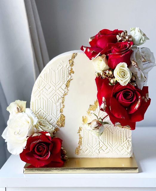 there is a white and red cake with flowers on the top, sitting on a table