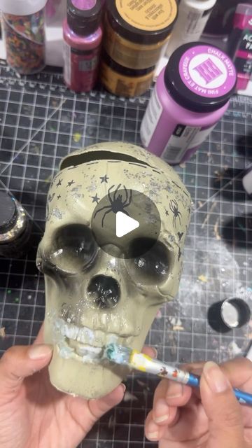 someone is painting a skull with paint on it's face and holding a brush