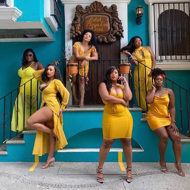 four women in yellow dresses standing on steps with their hands behind their backs, posing for the camera