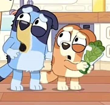 two dogs standing next to each other holding broccoli