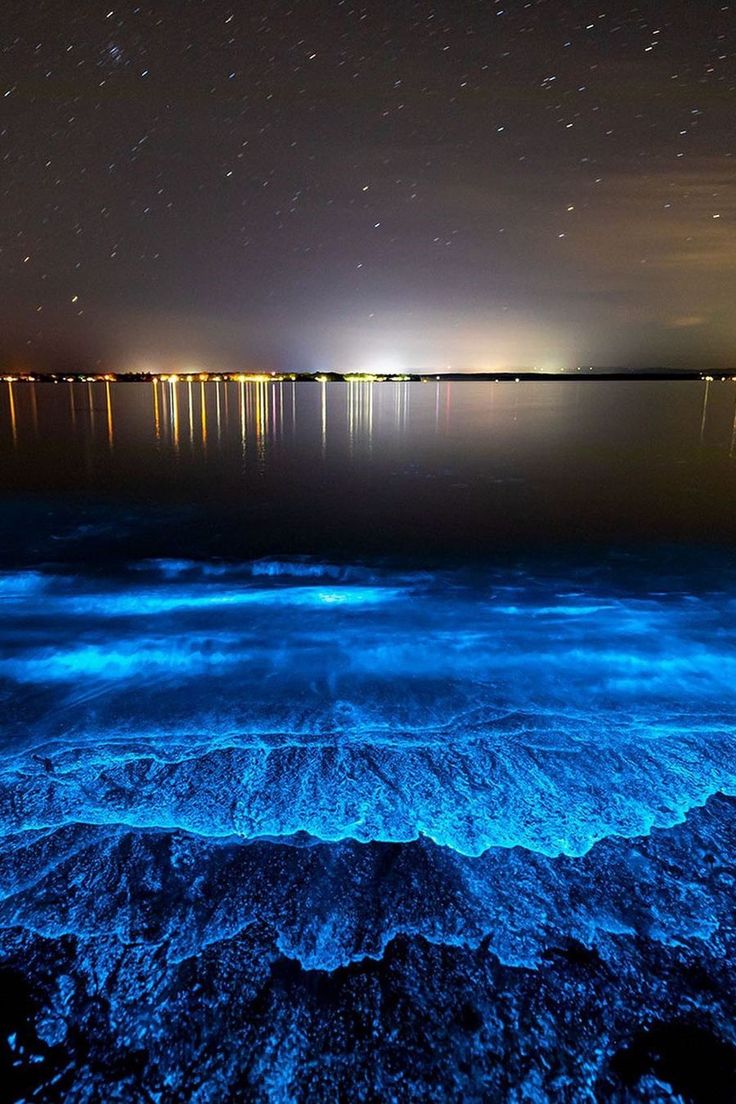 the night sky is lit up with bright lights and stars above water's surface