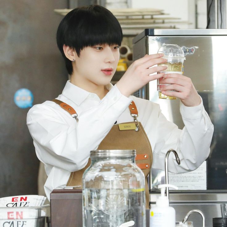 a young man holding a glass in his right hand while standing next to a counter