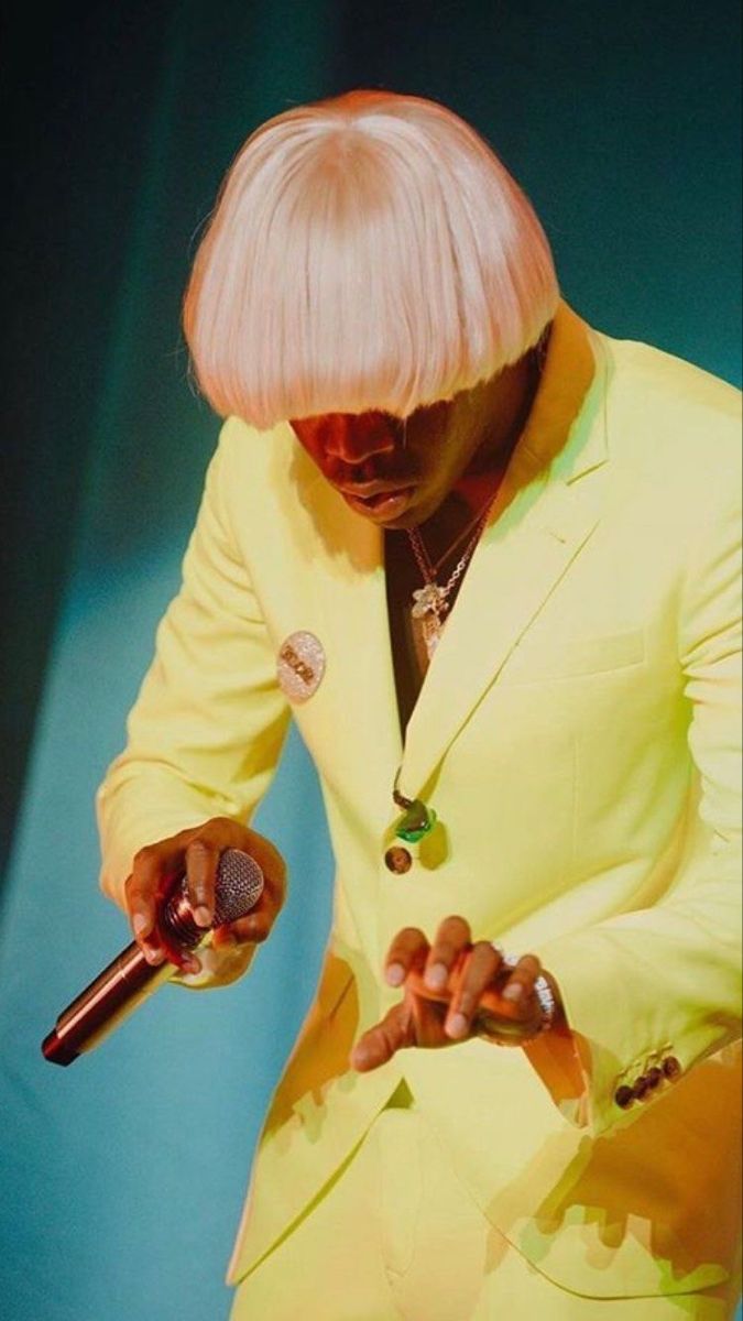 a man in a yellow suit is holding a microphone and looking down at his hand