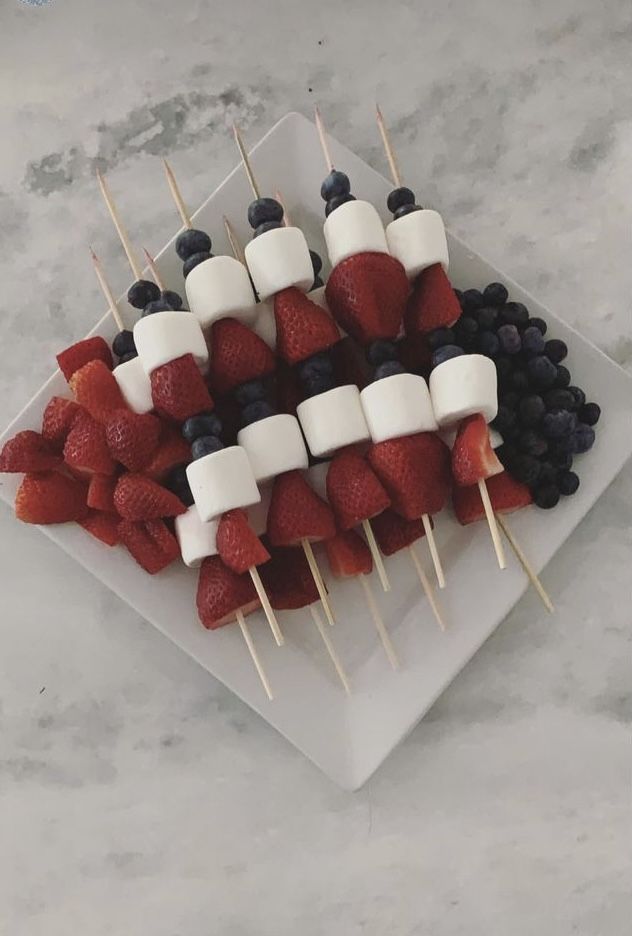 strawberries and blueberries are arranged on skewers with marshmallows