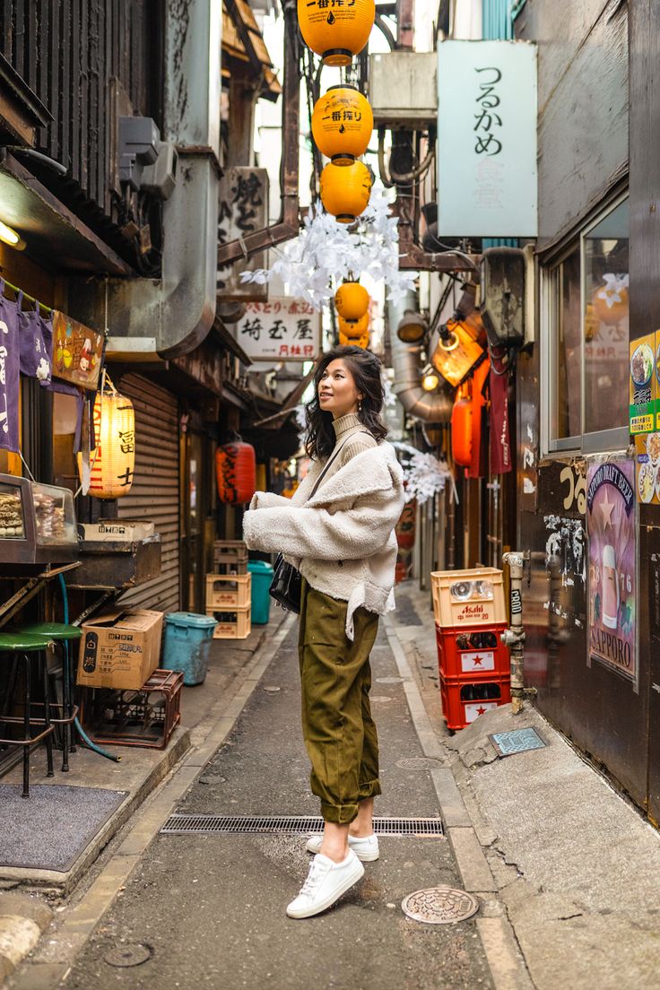 a woman standing in an alley way with lots of orange lanterns hanging from the ceiling