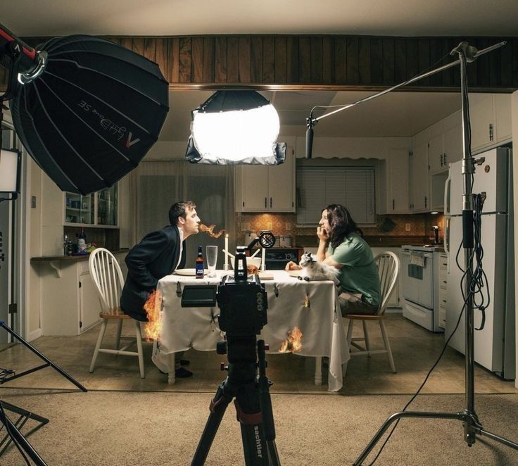 a man and woman sitting at a table in front of a camera set up for a photo shoot