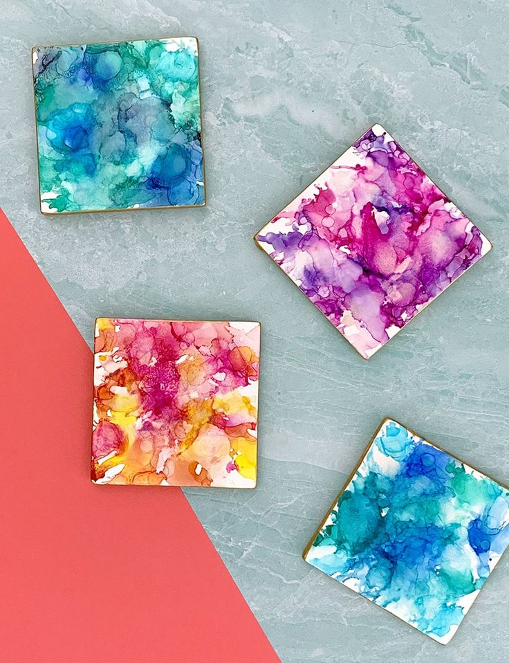 three square glass coasters with different colored designs on them and one is pink, blue, yellow, and green