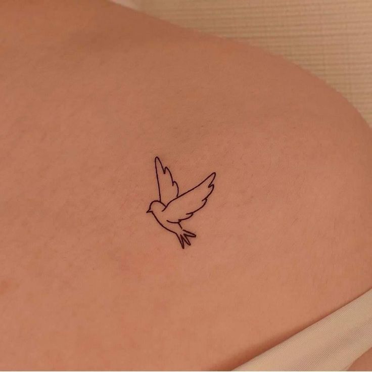 a small bird tattoo on the back of a woman's left arm and shoulder