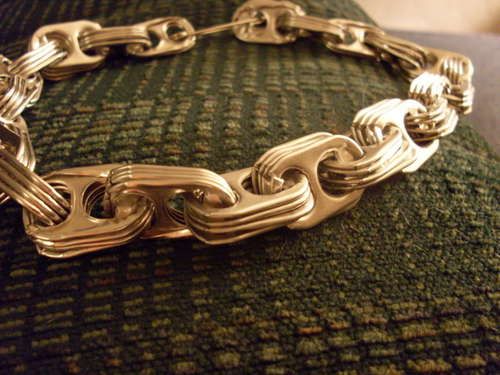 a close up of a gold chain bracelet on a green cushion with the clasp undone