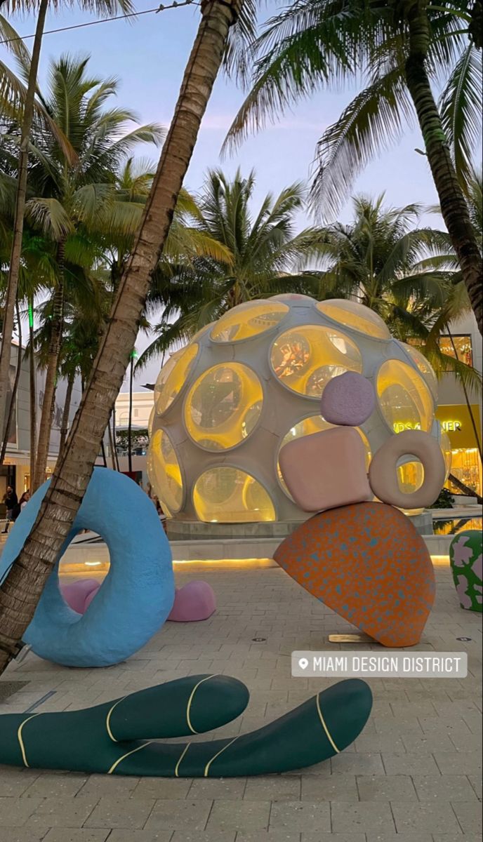 an outdoor sculpture in the shape of a ball and fish with palm trees around it