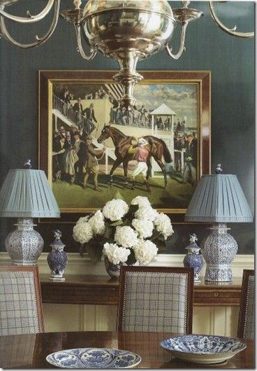 a dining room table with blue and white plates on it, vases in front of a painting