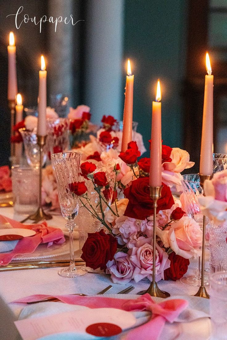 a table topped with lots of pink and red flowers next to tall candle holders filled with wine glasses