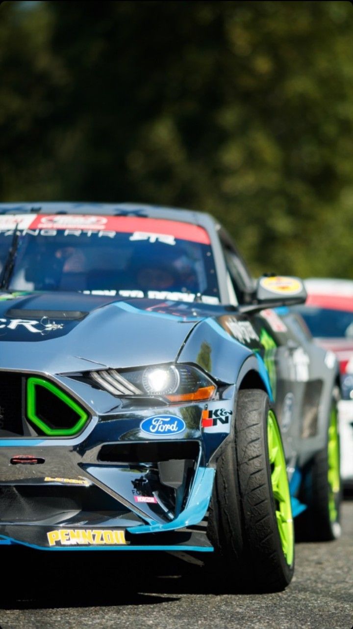 two racing cars driving down the road with trees in the background