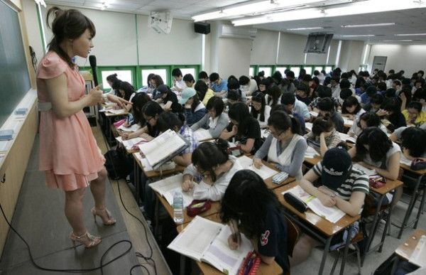 a woman standing in front of a class room full of students sitting at desks