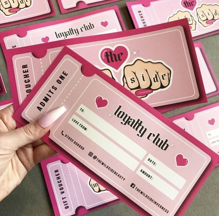 a person holding up some pink tickets with hearts on them and two fingers pointing at the ticket