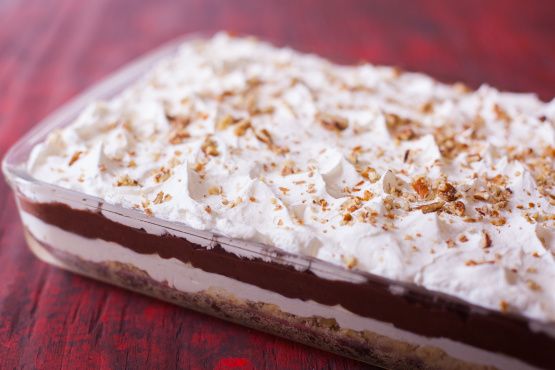 a chocolate dessert with white frosting and chopped nuts on top is sitting on a red table