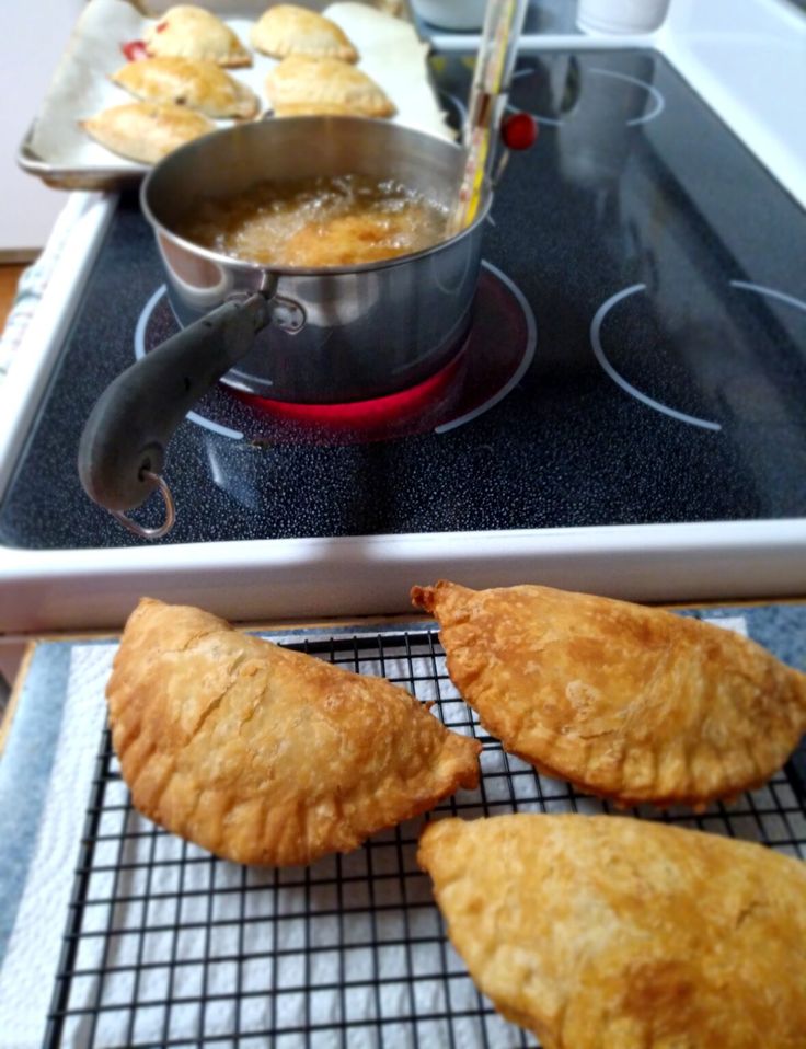 three pastries sitting on top of a stove next to a pan filled with food