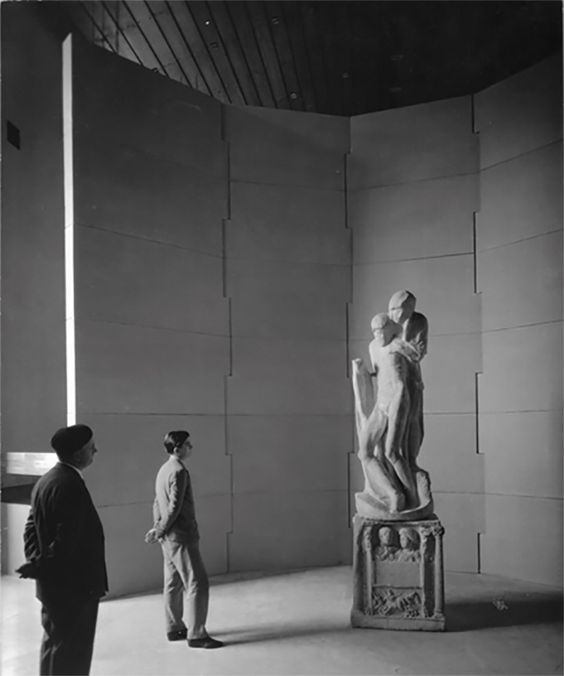 two men standing next to a statue in a room with white walls and ceilinging