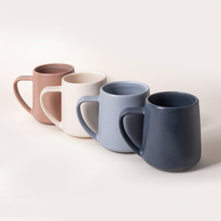 three different colored coffee mugs lined up on a white surface, one is blue and the other is pink