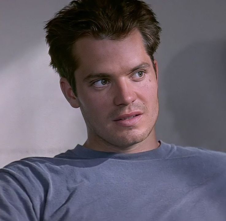 a close up of a person wearing a gray shirt and looking at the camera with an intense look on his face