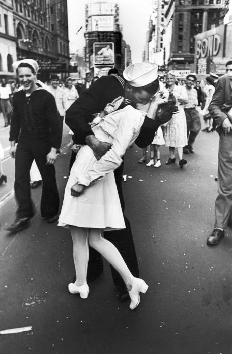 an old photo of a man and woman kissing on the street with people in the background