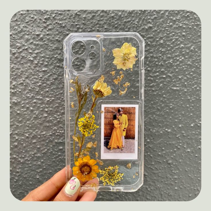 a person holding up a phone case with flowers and a photo on the back, in front of a gray wall