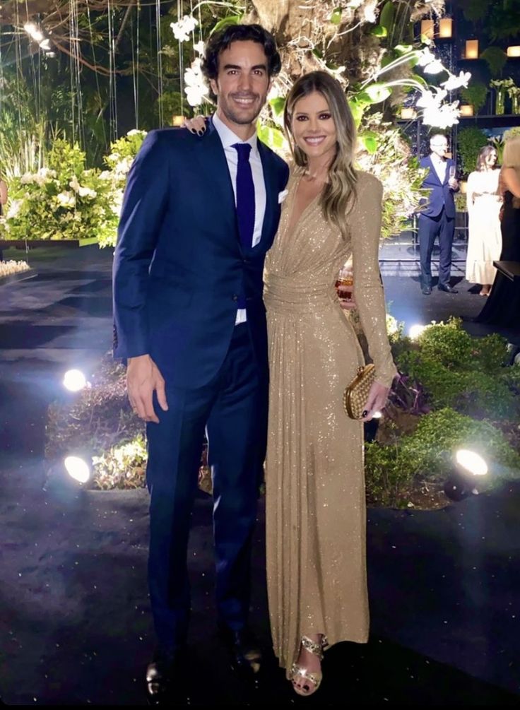 a man and woman standing next to each other in front of a garden at night