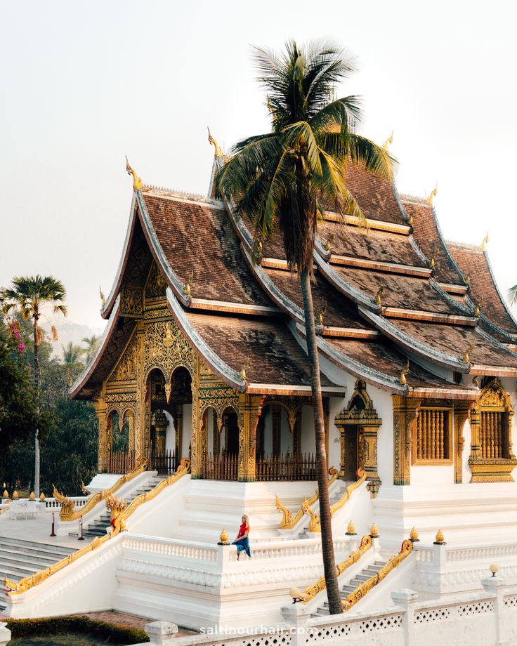 a white and gold building with steps leading up to the top floor, next to a palm tree