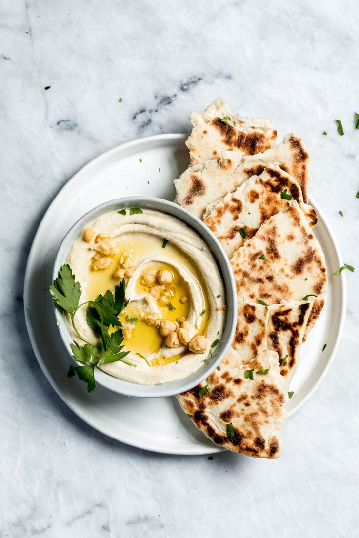 a white plate topped with pita bread next to a bowl filled with hummus