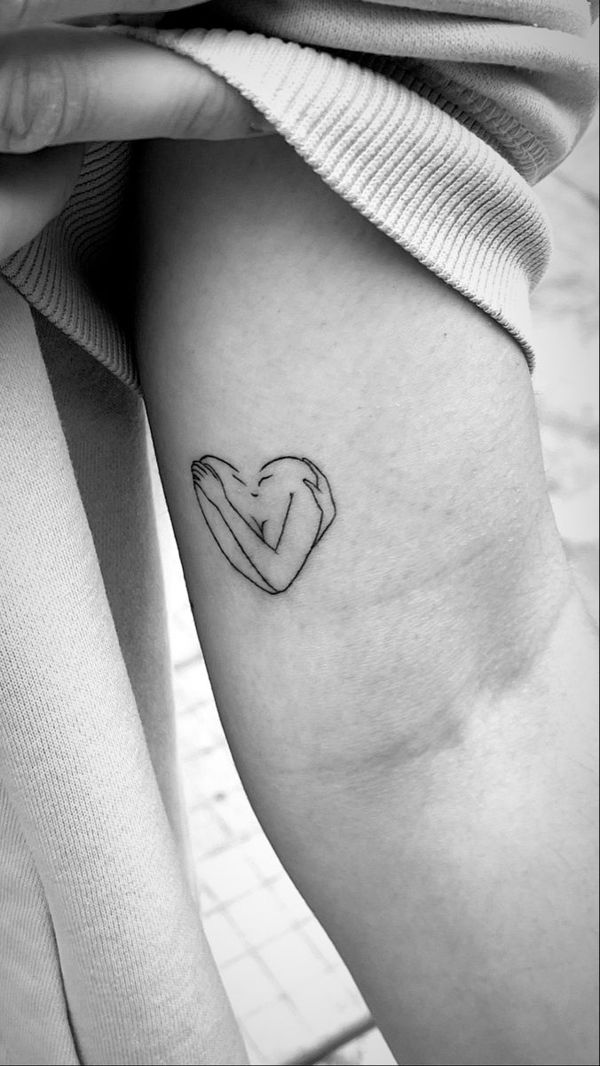 a woman's arm with a small heart tattoo on the left side of her thigh