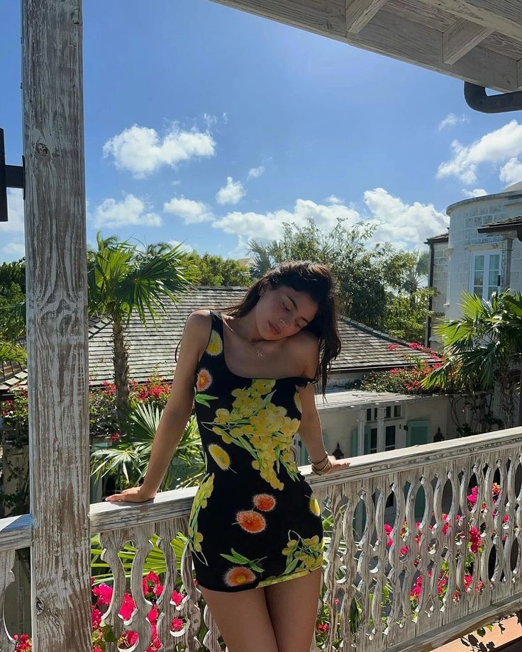 a woman standing on a porch next to a white fence with flowers in the background