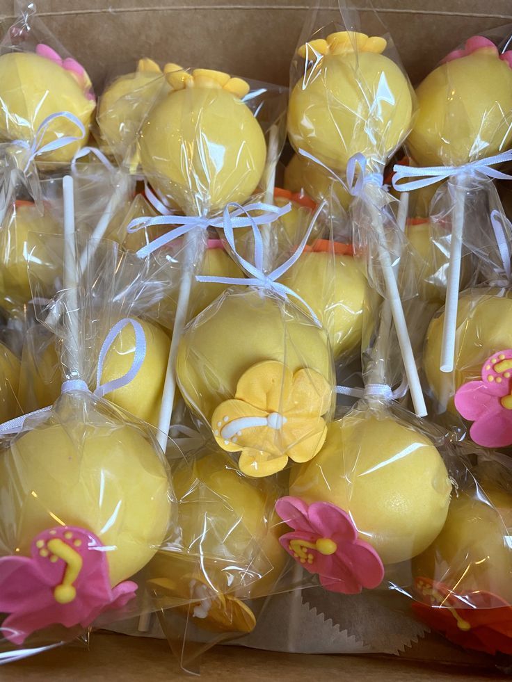 some yellow cake pops with pink flowers on them in plastic wrappers and wrapped in cellophane