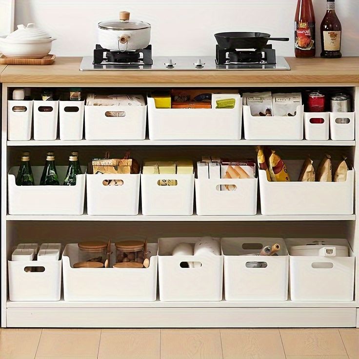 an organized kitchen with white bins on the bottom shelf and lots of containers below