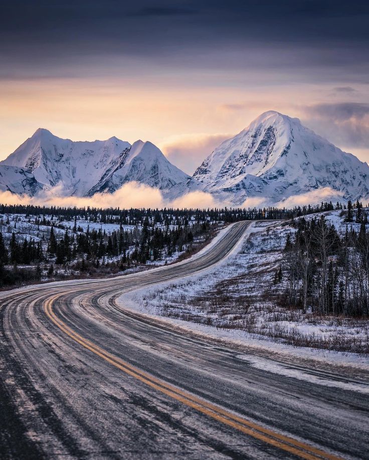 an empty road in front of snow covered mountains