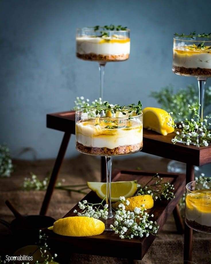 two desserts with lemon slices and flowers in them on a wooden table next to some glasses