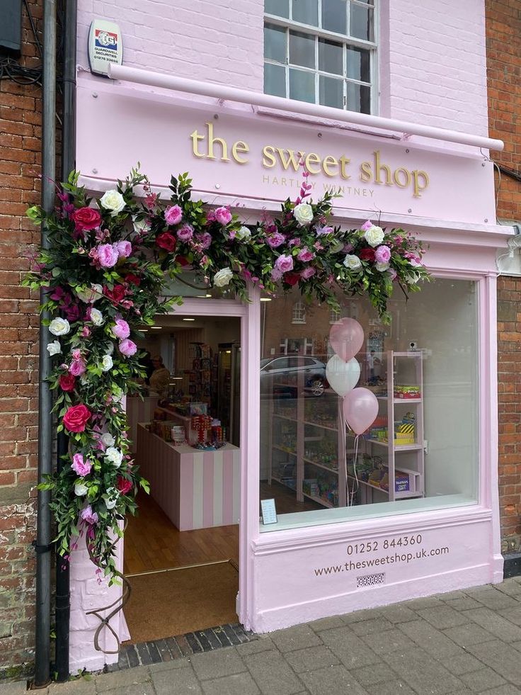 the flower shop is decorated with pink flowers and white balloons in front of the store