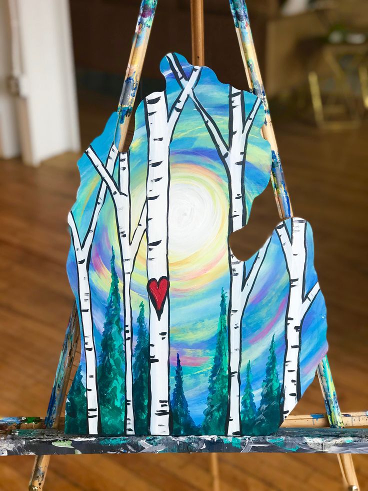 an easel painted with birch trees and a heart on the back, sitting on a wooden floor