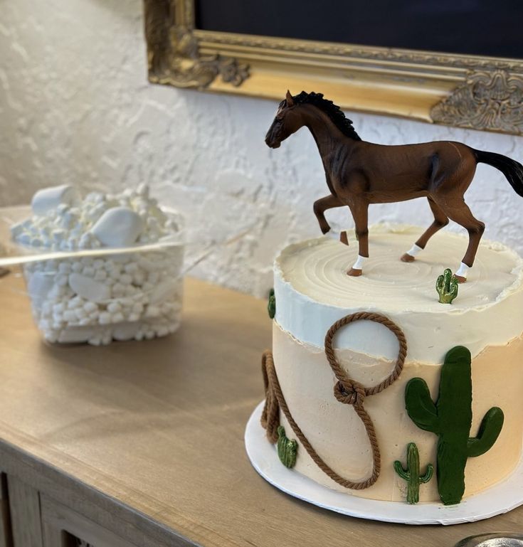 a small horse is on top of a white cake with green icing and cactus decorations