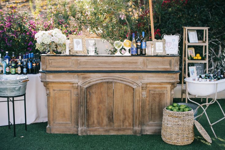 an outdoor bar is set up with flowers and bottles on the table for guests to drink