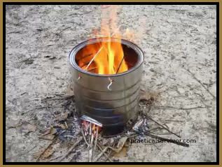 an open barrel sitting on top of a sandy beach next to a campfire with sticks sticking out of it