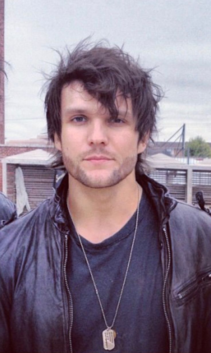 a man in a leather jacket is posing for the camera with his hair blowing in the wind