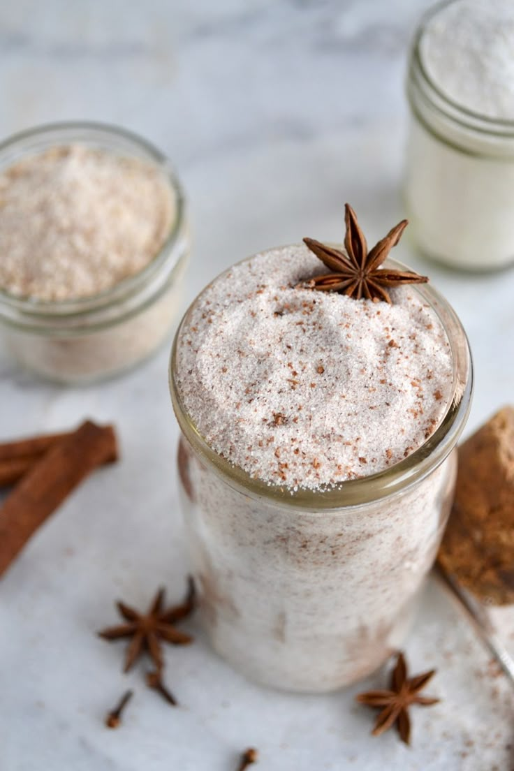 two jars filled with different types of spices on top of a white counter next to cinnamons and star anise