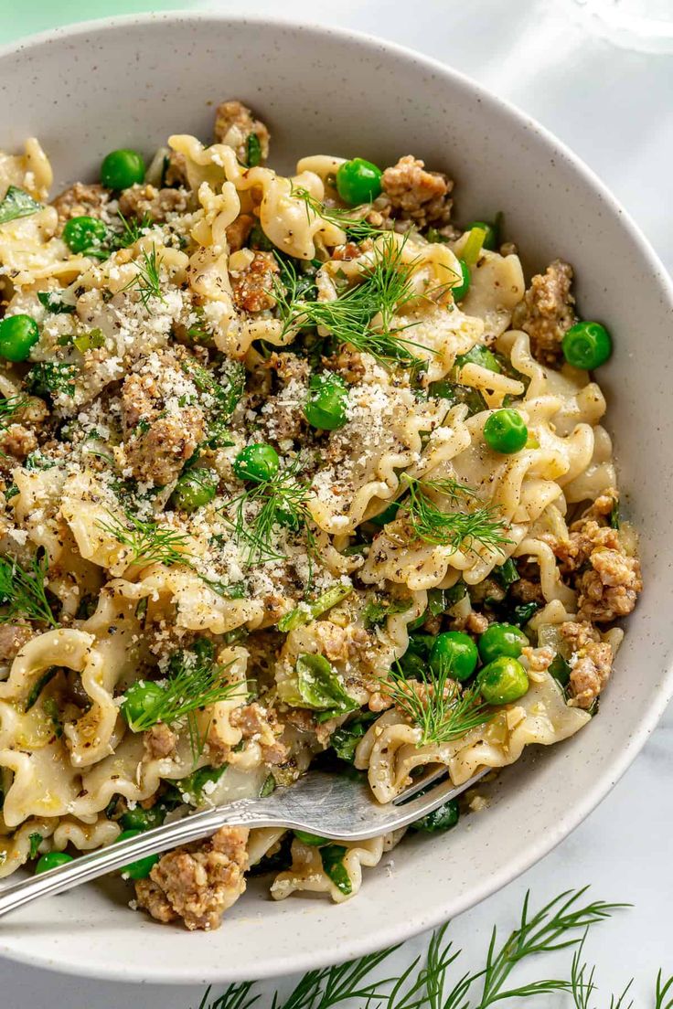 a bowl filled with pasta, peas and meat on top of a white table cloth